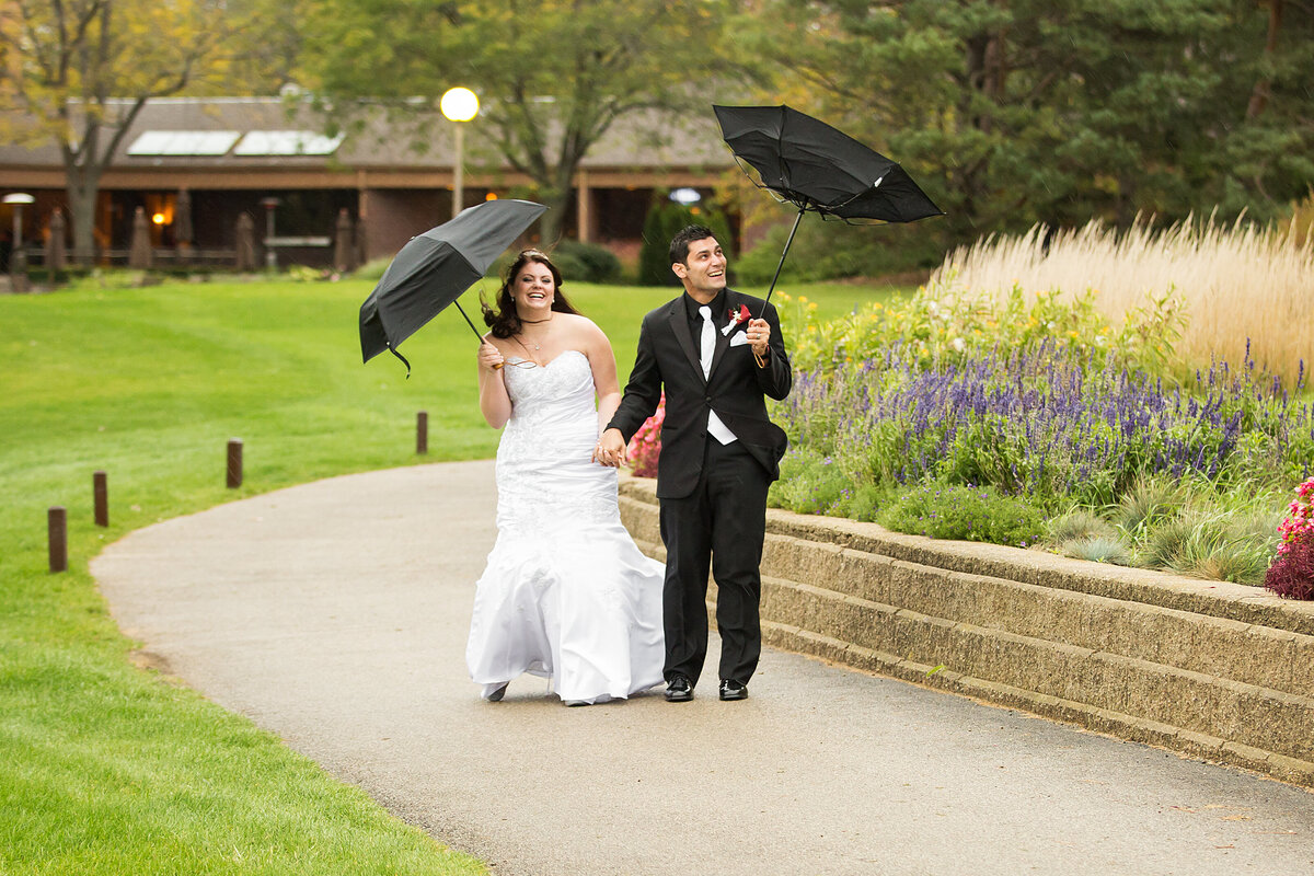 An outdoor wedding photo with umbrellas on a rainy day.