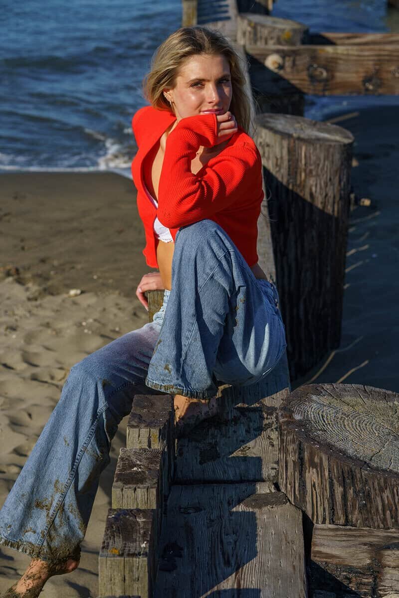 Young woman in wet jeans and a skimpy top sitting on a wooden pier at the beach