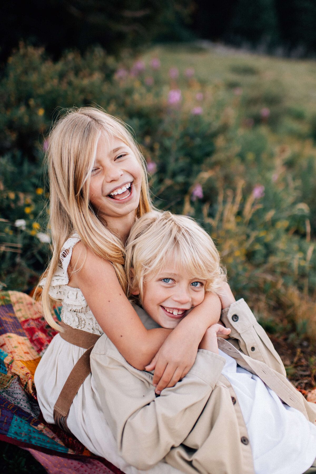 sister hugging her younger brother in a wildflower field while they laugh with the photographer