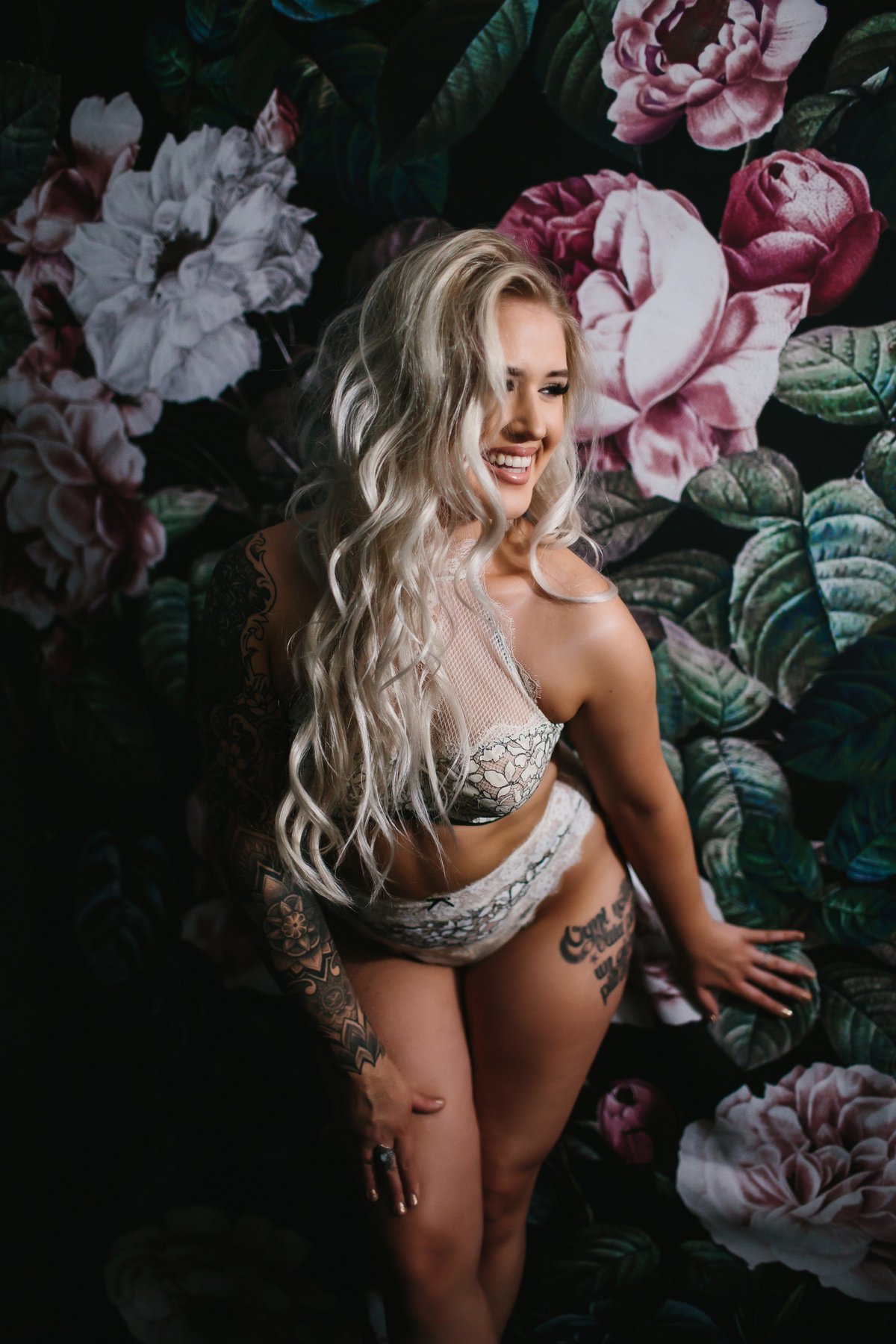 Blonde woman in white lace lingerie set posing against floral backdrop