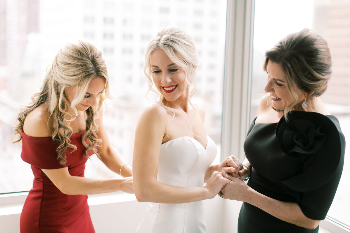 bride's sister buttoning dress while holding mother's hands