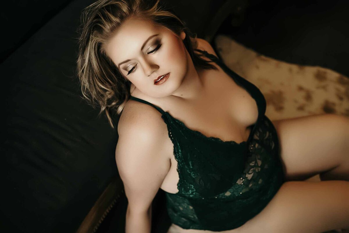 Blonde curvy woman in dark green lingerie posing for boudoir shoot