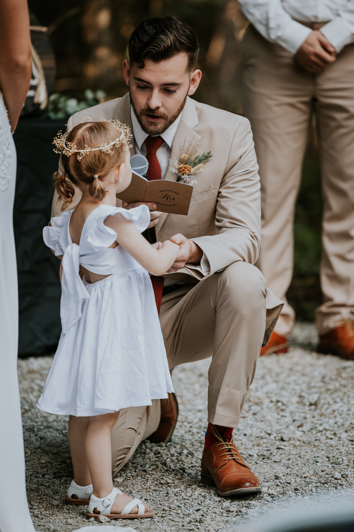Groom leans on one knee while reading vows to brides daughter.
