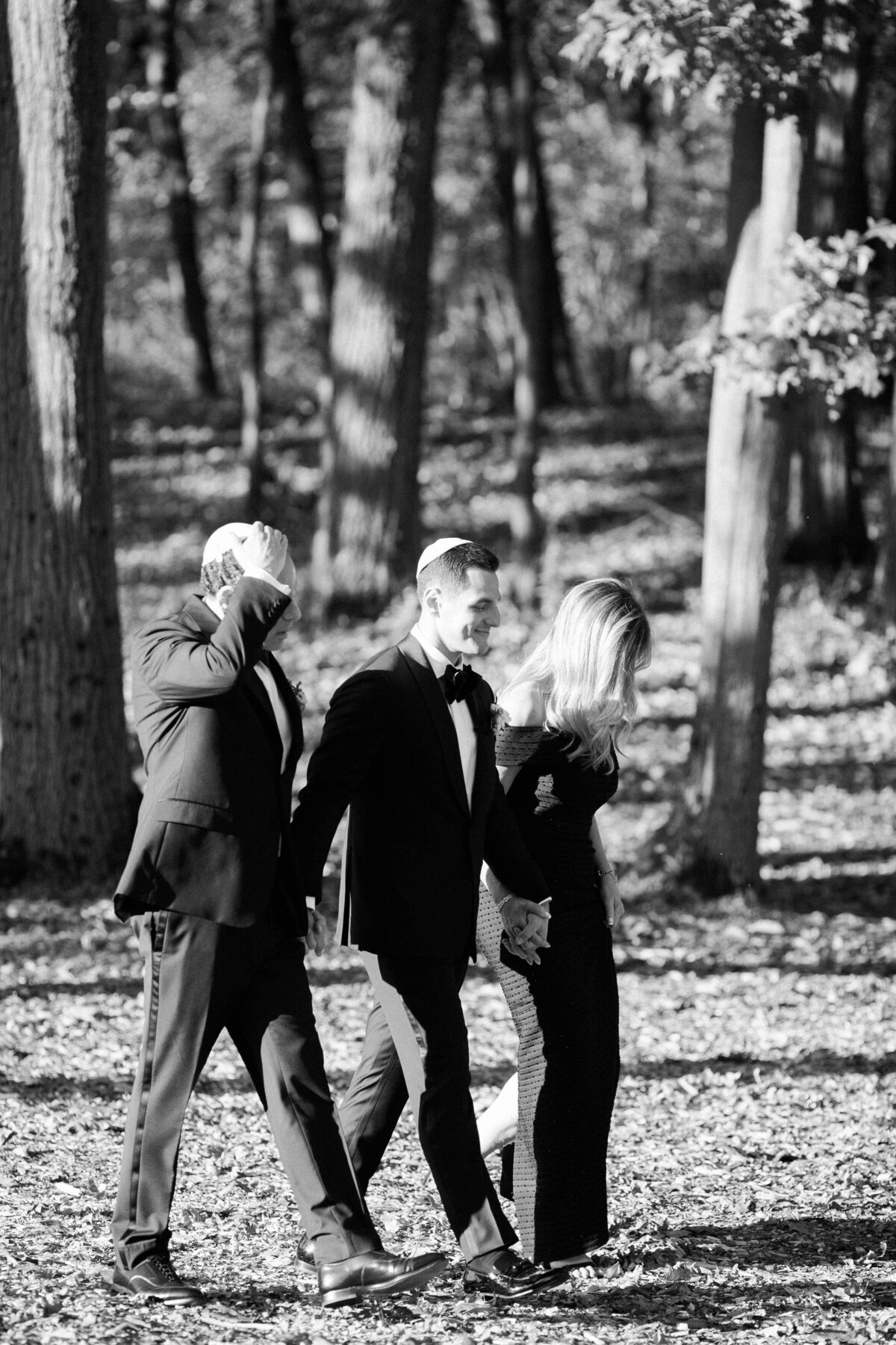 the groom walking hand-in-hand with a woman in a black gown and another man in a tuxedo