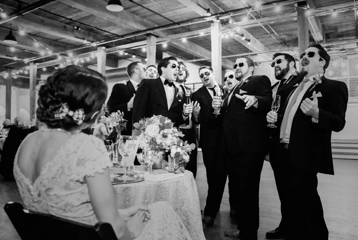 Groomsmen sing along to a performance, the bride seated at the foreground