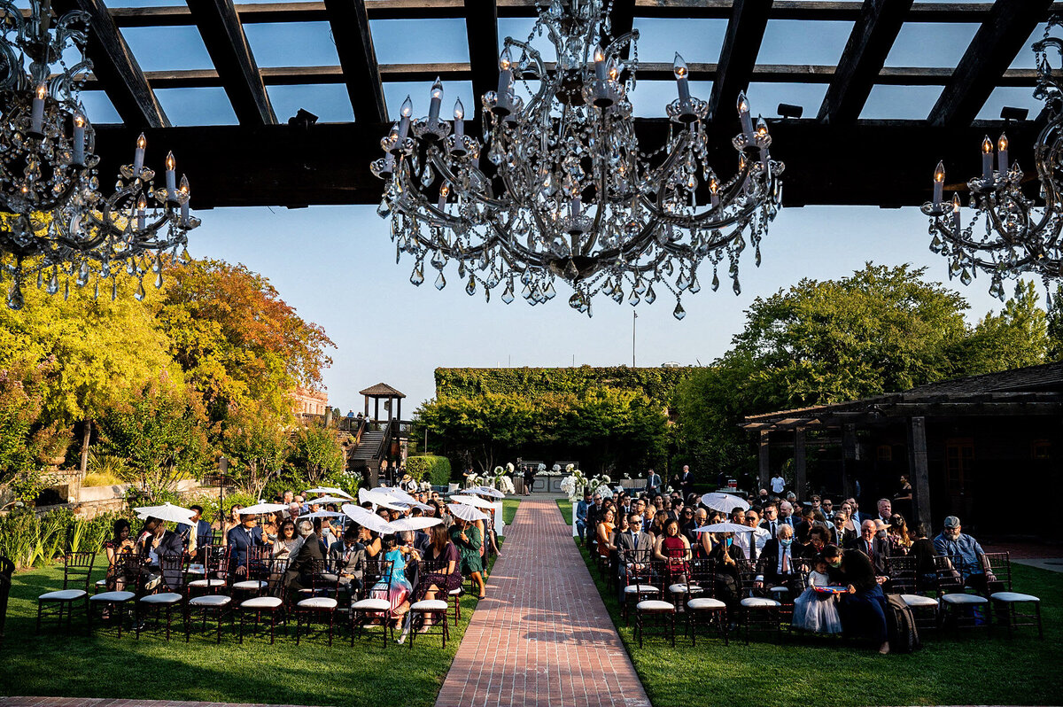 San Francisco Bay Area wedding photographer documents outdoor ceremony with elegant crystal chandelier pergola and brick aisle surrounded by wedding guests at Estate Yountville in Napa Valley