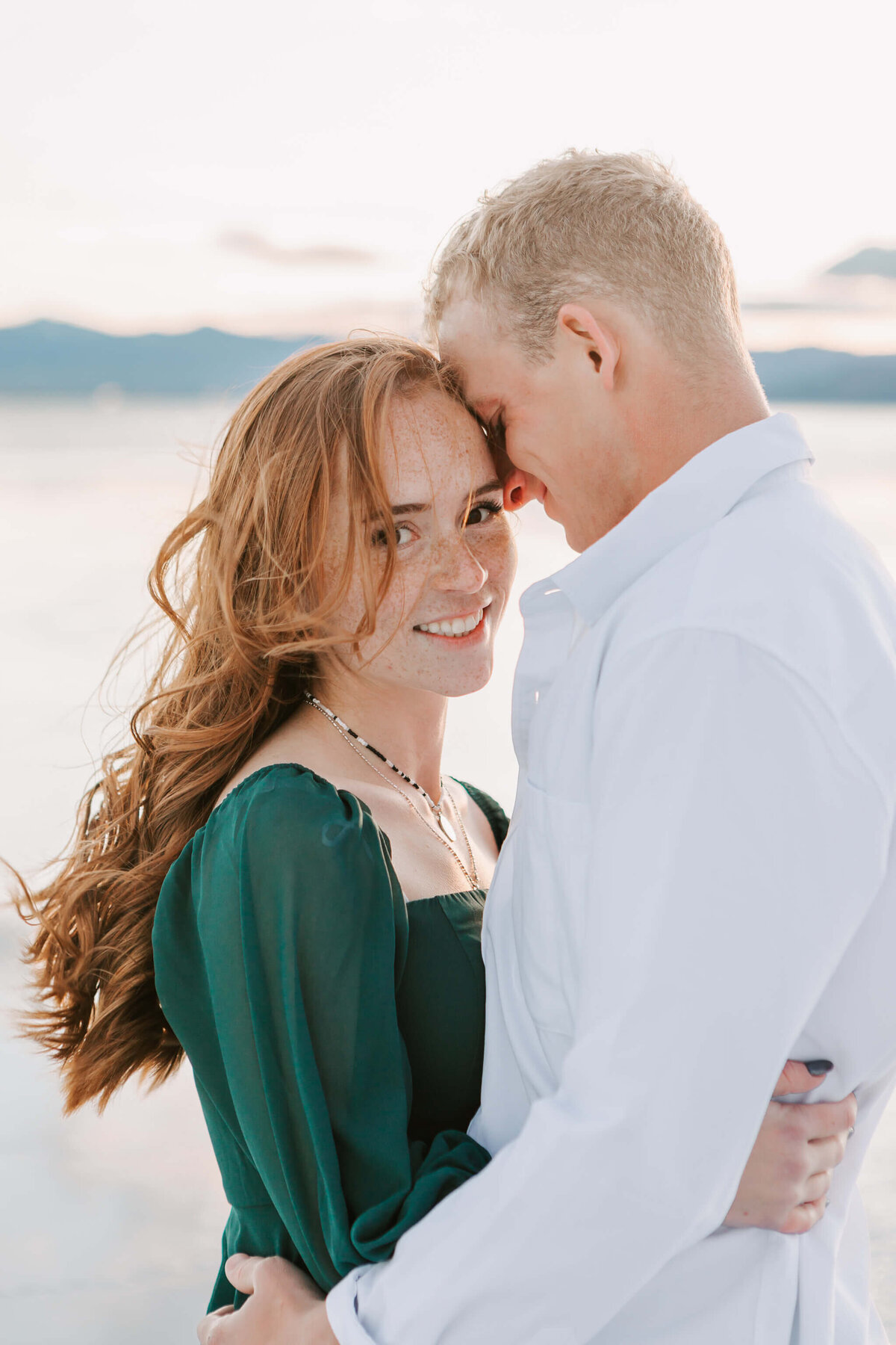 An engaged couple stands smiling and hugging on the salt flats in Bonneville, UT