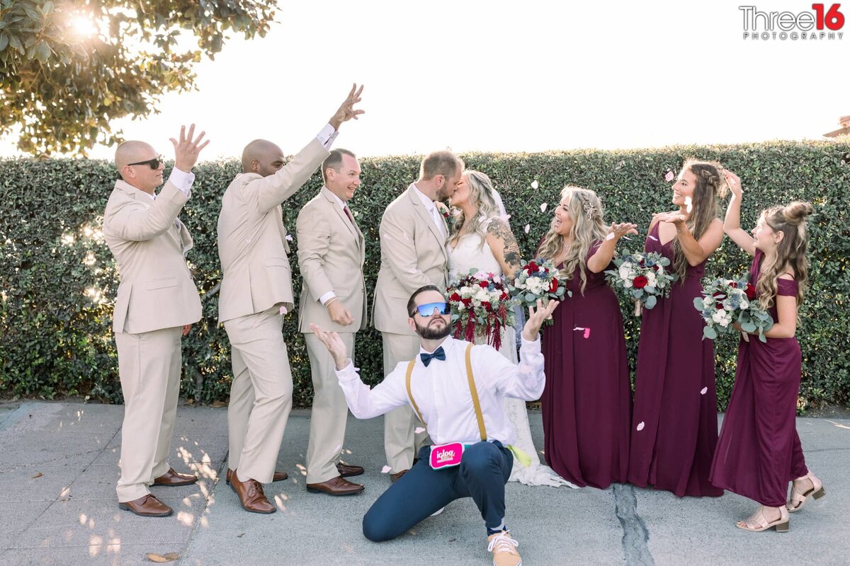 Bridal party goofs off around the newly married couple as they share a kiss