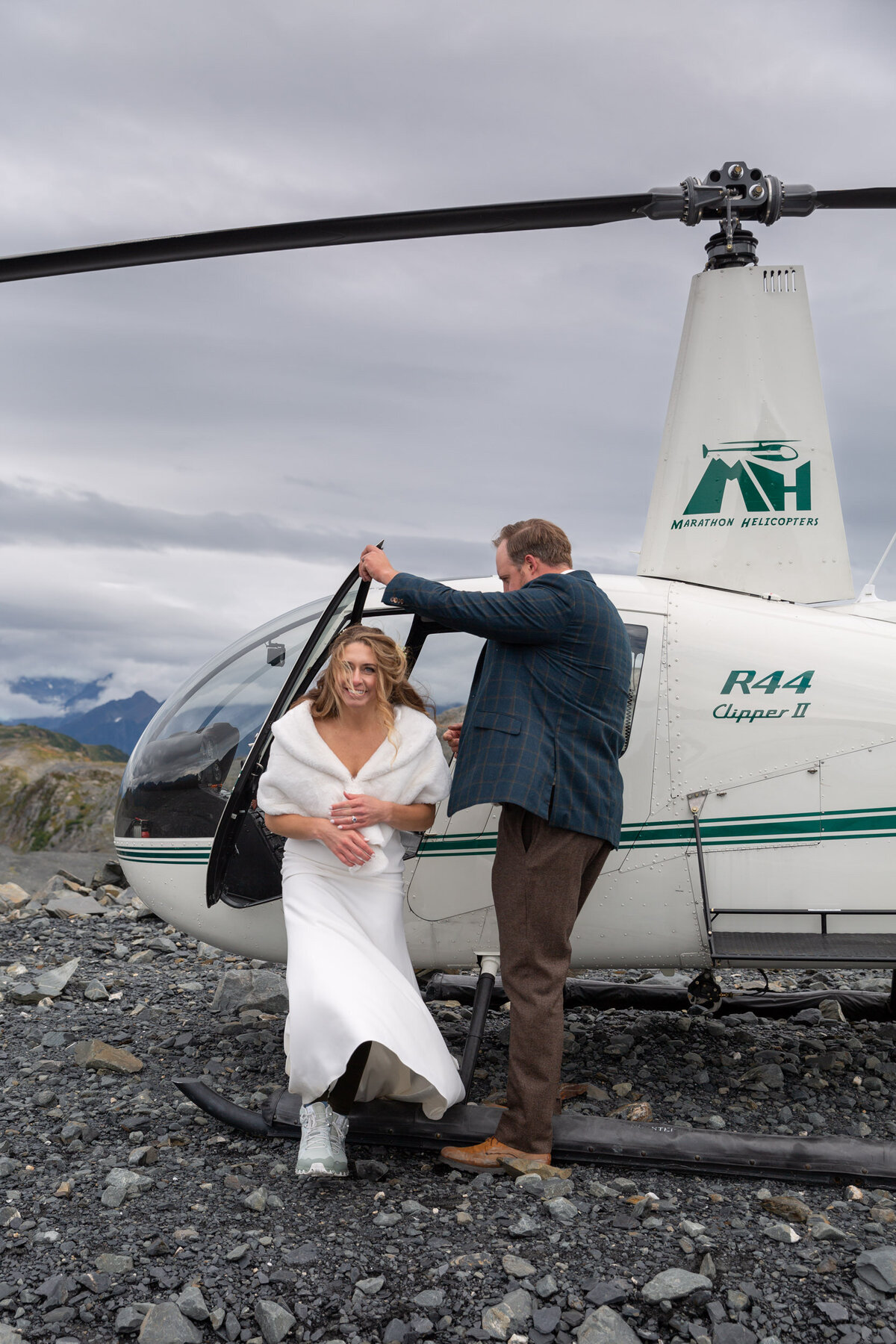 A groom holds the helicopter door open for his Bride as she steps out.