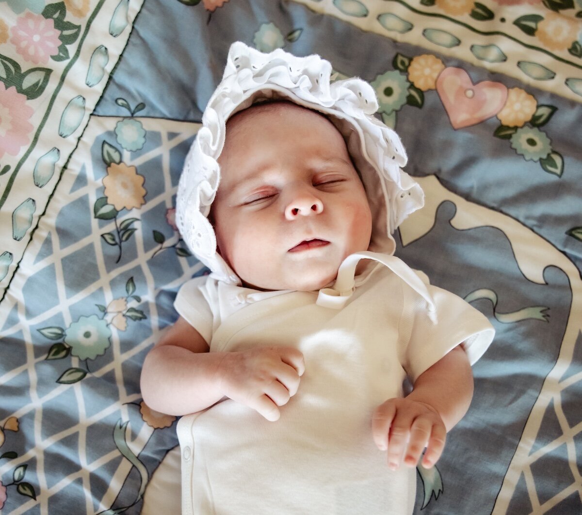 a baby girl wearing a bonnet sleeping on a bed