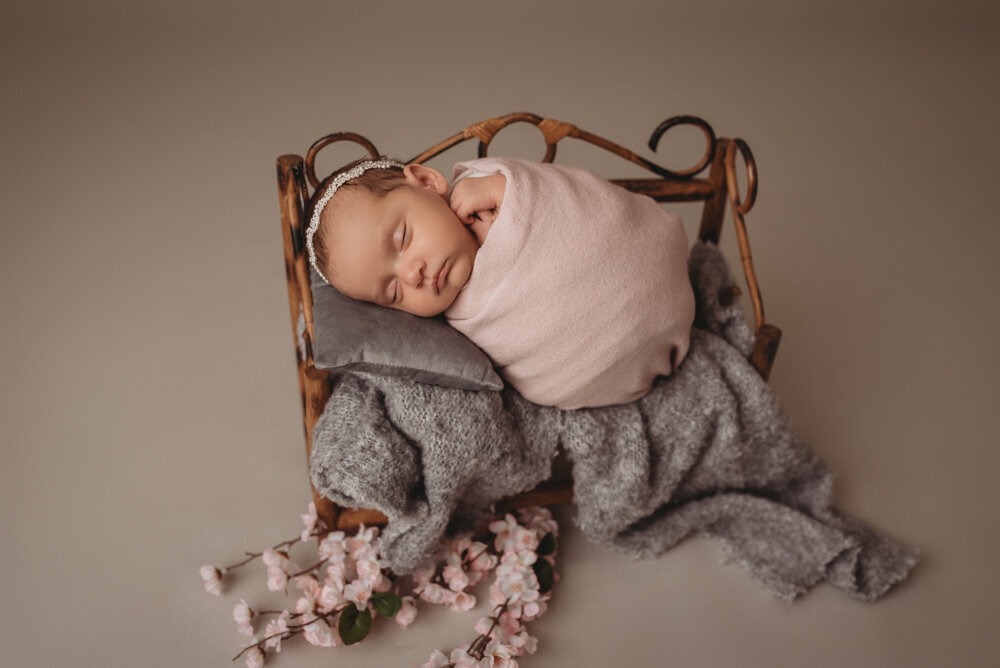 Newborn photo shoot photographed by Atlanta, Georgia newborn photographer with baby posing on neutral fabric with dainty headband on and sleeping on tiny bench.