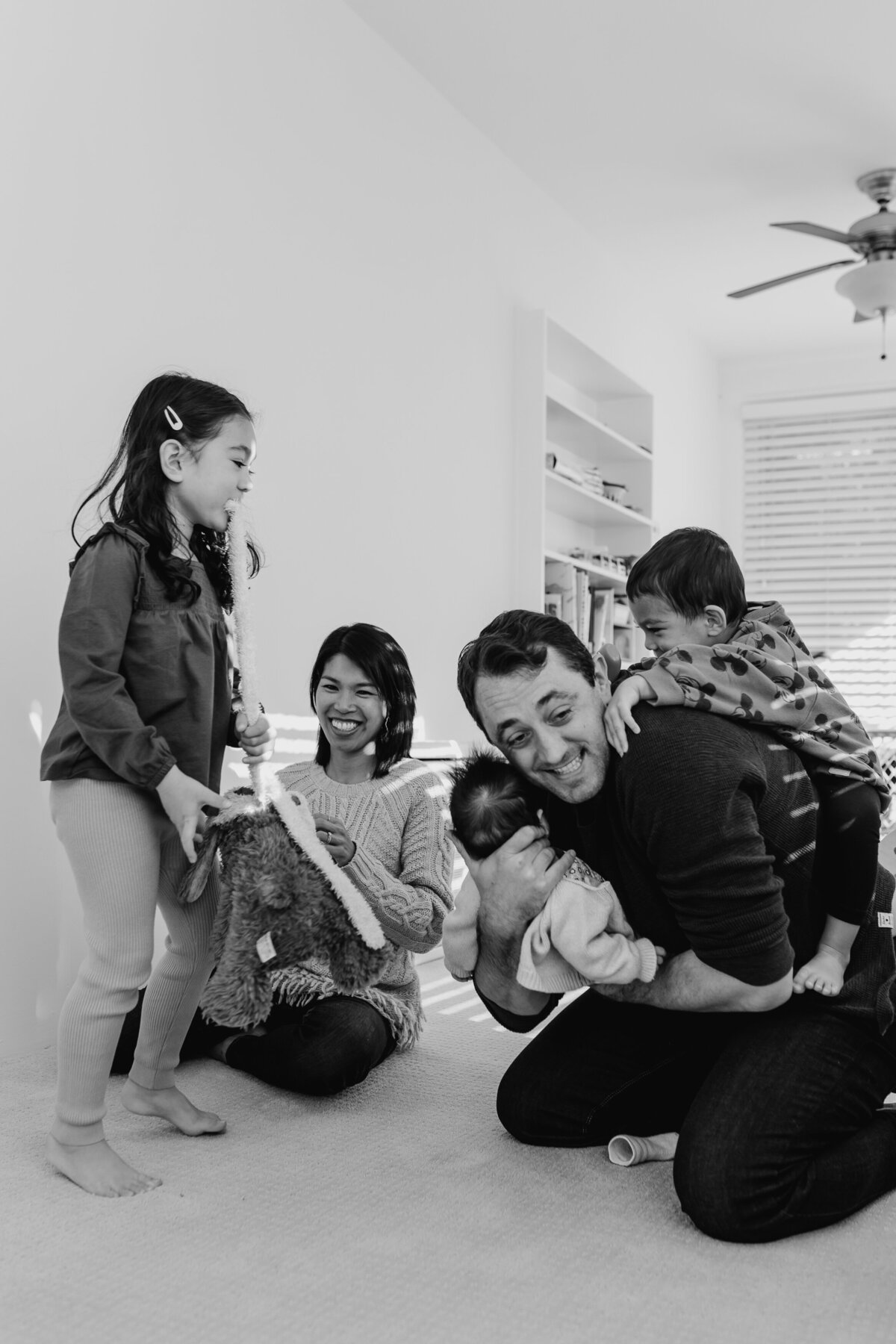 Family Photographer,  a mom and dad laugh and play with their kids  inside, dad holds newborn baby