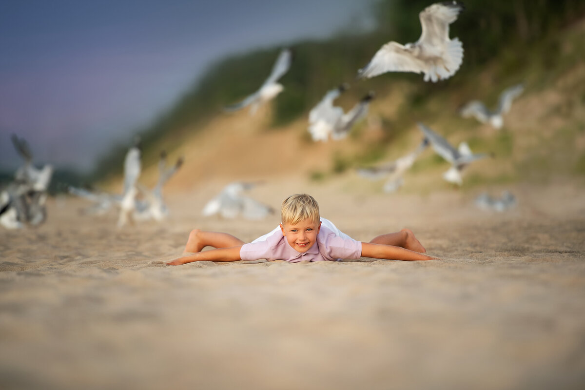 Little boy running with seagulls and rolling on Indiana dunes National Park sand.