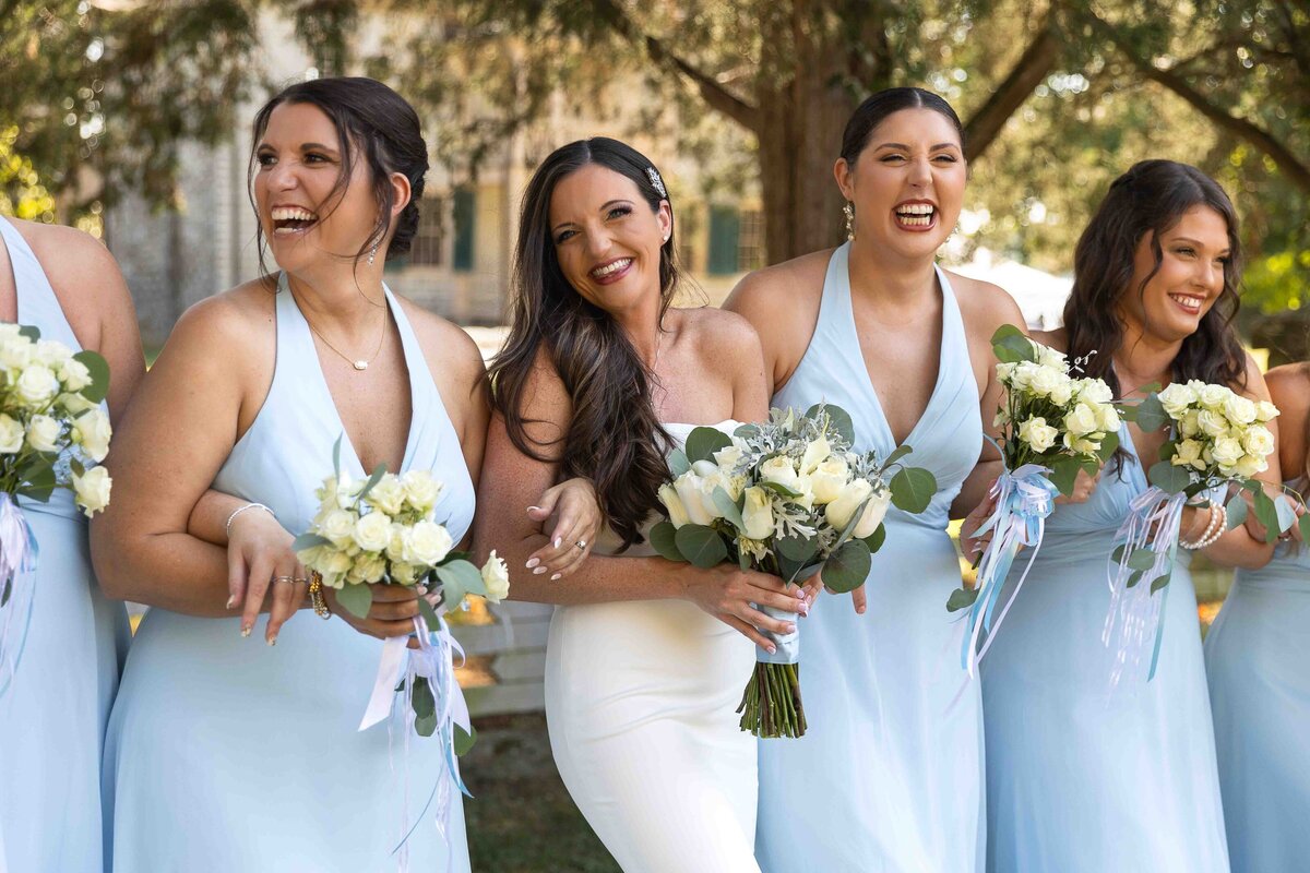 Bride laughing with bridesmaids all holding bouquets 