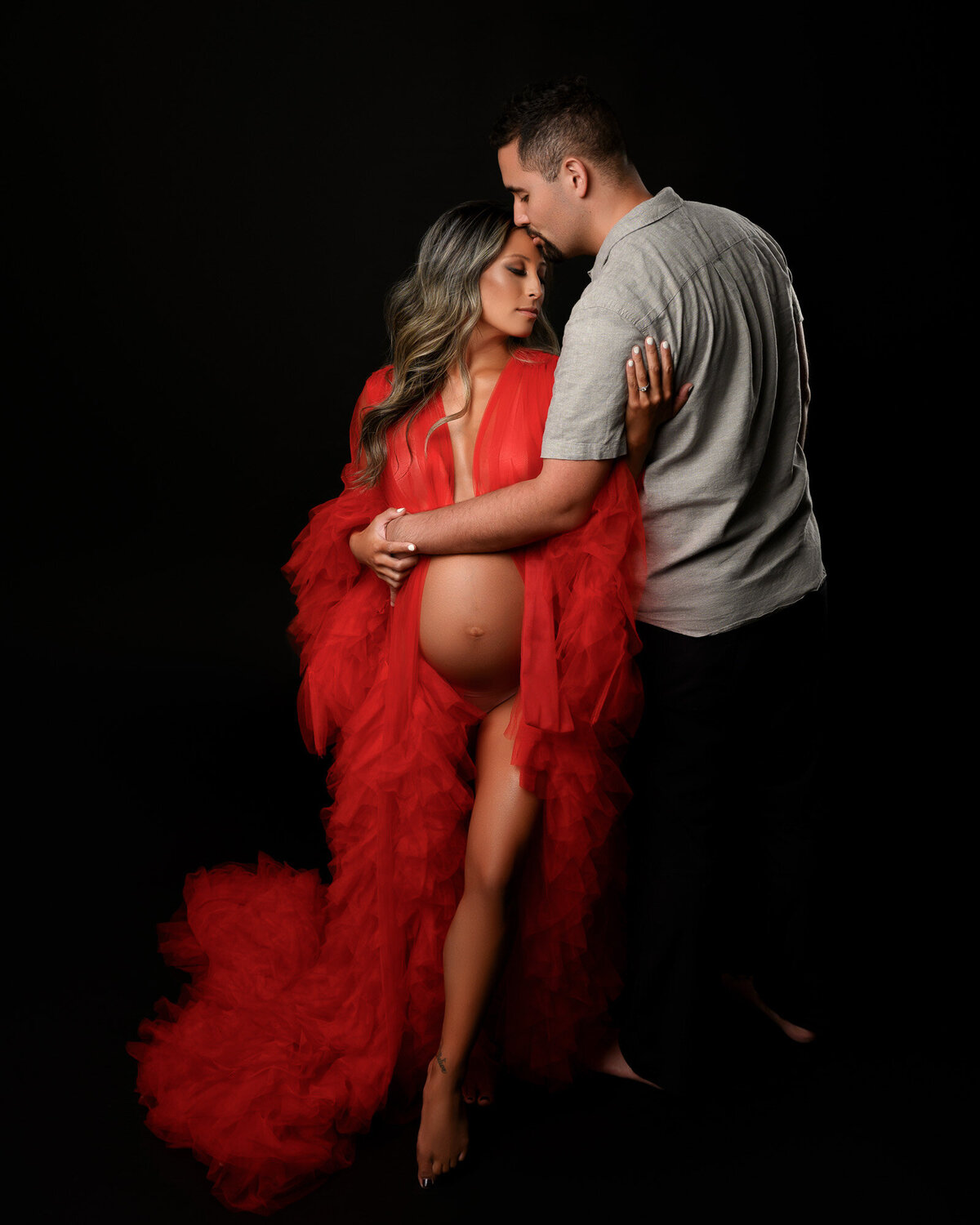 Dramatic maternity portrait featuring pregnant woman in flowing red gown with artistic studio lighting