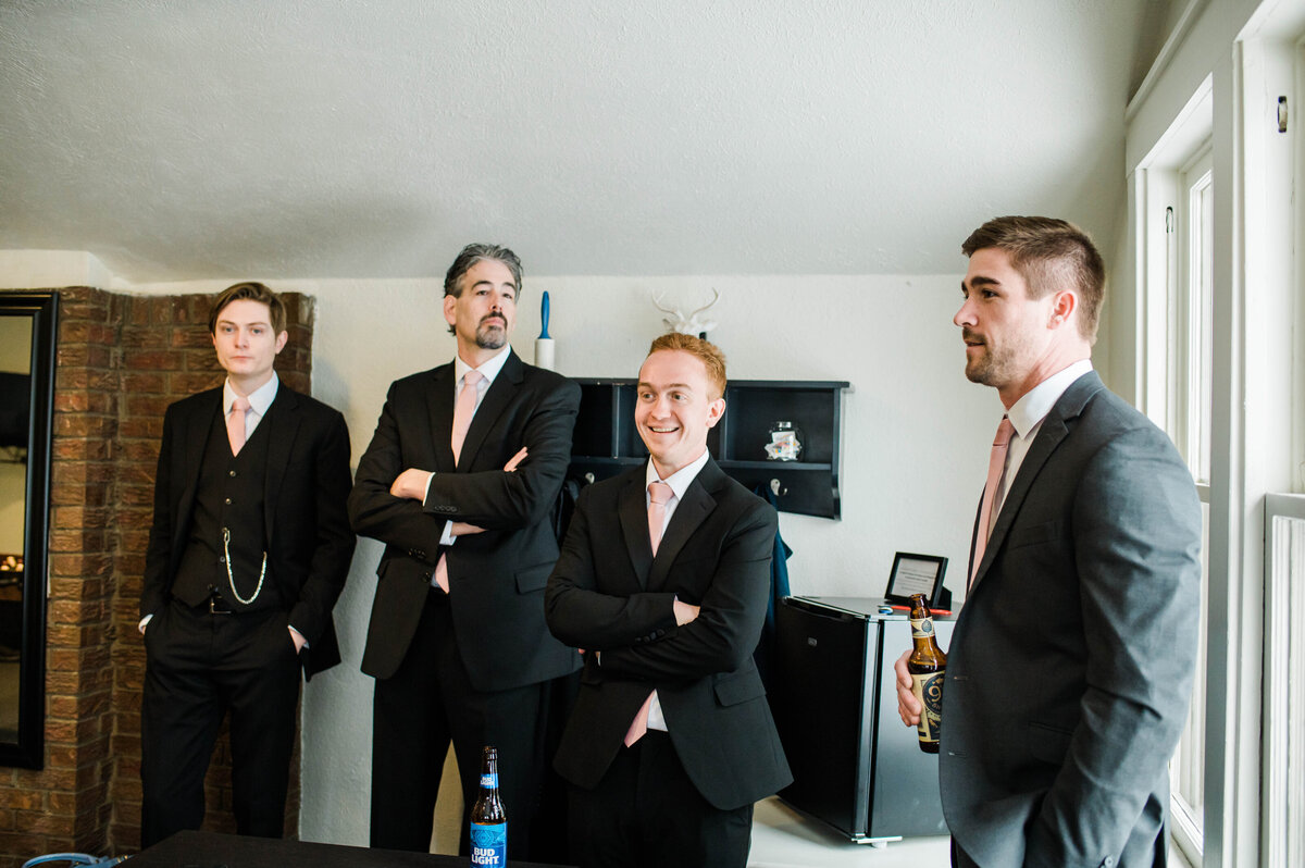 groomsmen stand in the grooms room while getting ready