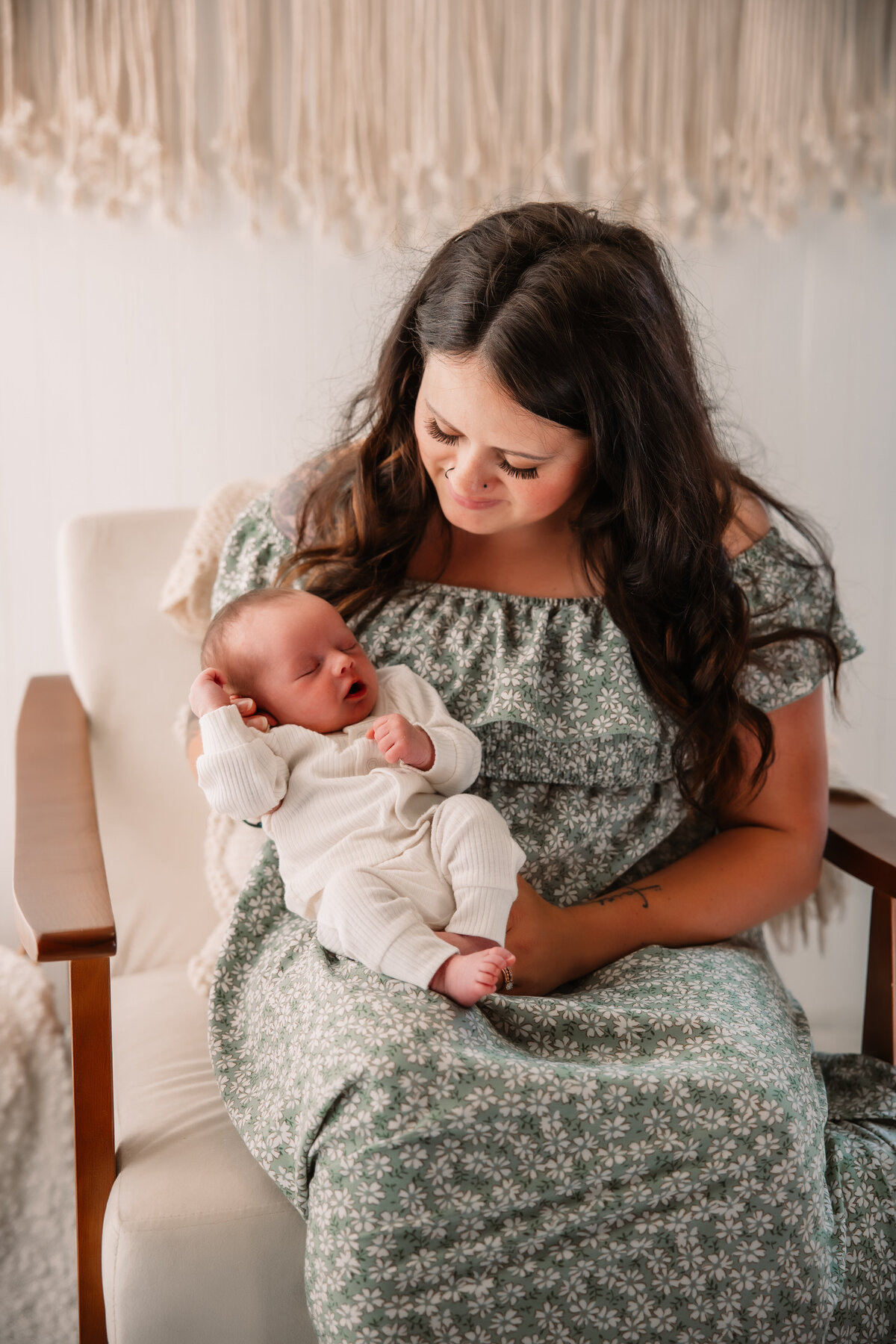 A happy mother in a green floral print dress sitting in a chair holding her newborn baby in her lap