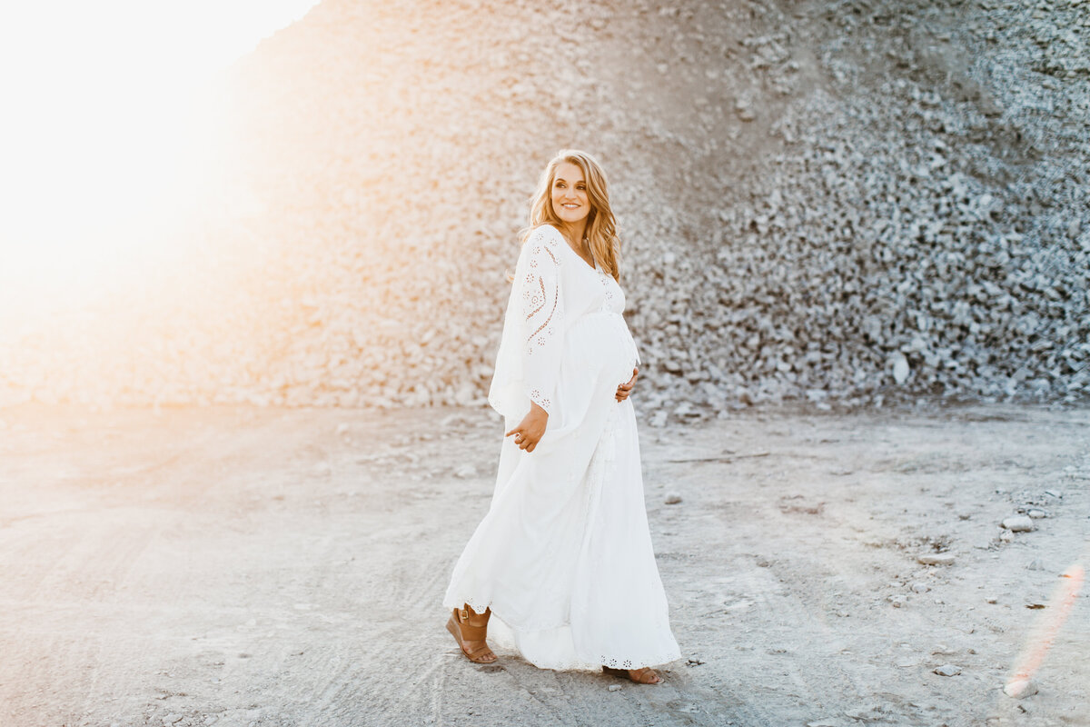 mom in white dress walking in sand for maternity session
