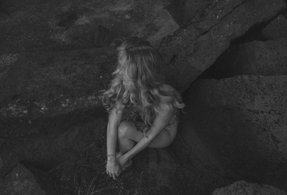woman with long blonde hair sits on rocks in Bend, Oregon