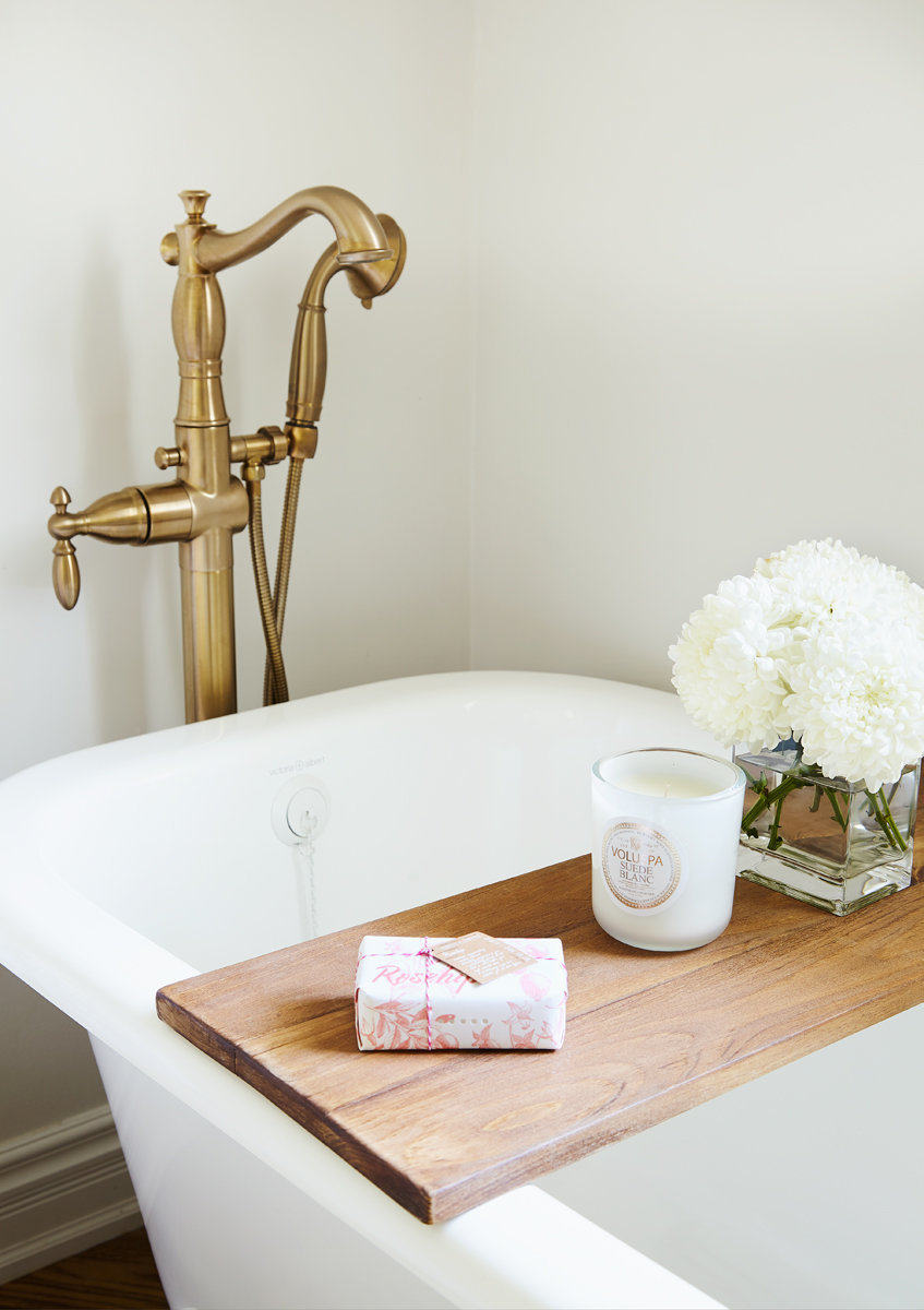 clawfoot bathtub with wood caddy and gold faucet in white Burlington bathroom