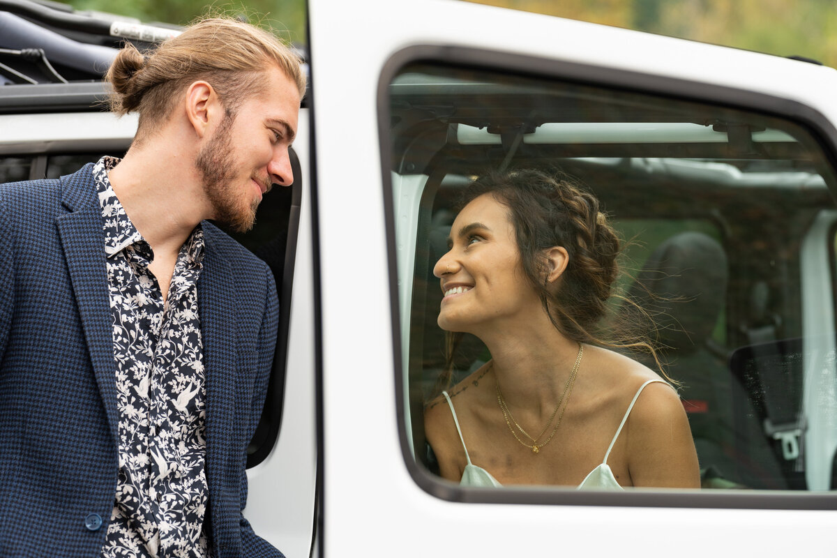A person sitting in a car smiling at their partner who is standing next to them