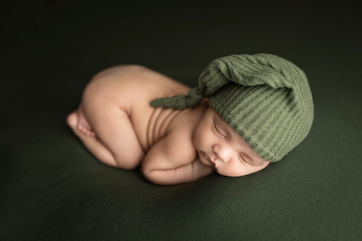 Newborn boy wearing a sage green sleepy cap.