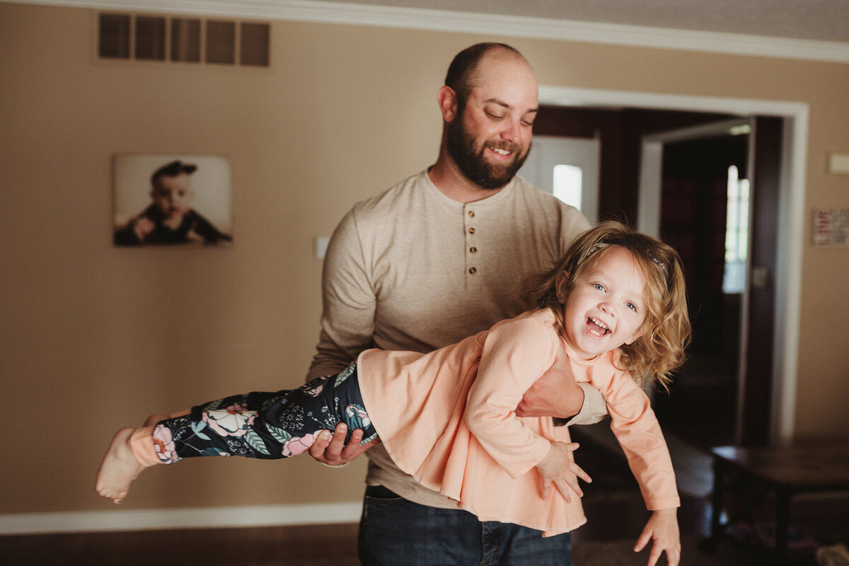Father "flying" his daughter like an airplane while laughing together.