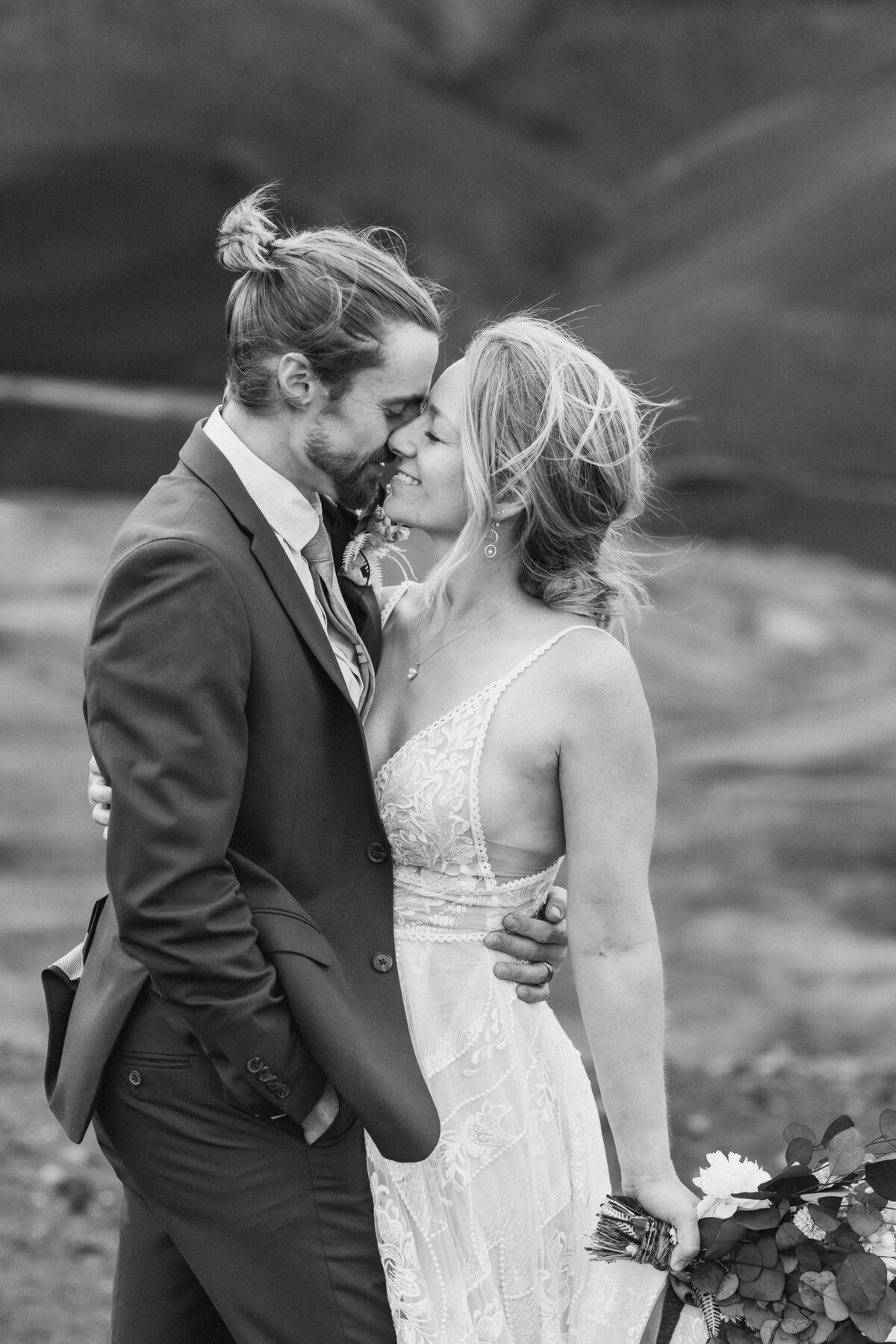 Black and white image of a couple on their wedding day about to kiss each other with their hair blowing in the wind.