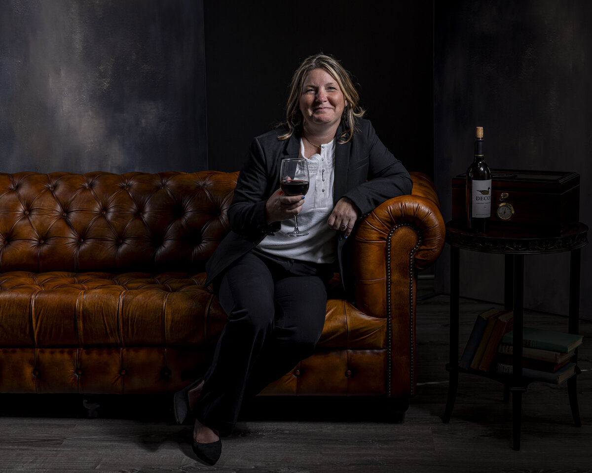 Branding portrait in CT of woman seated on brown leather sofa, holding coffee cup, by Rob Faber Photography.