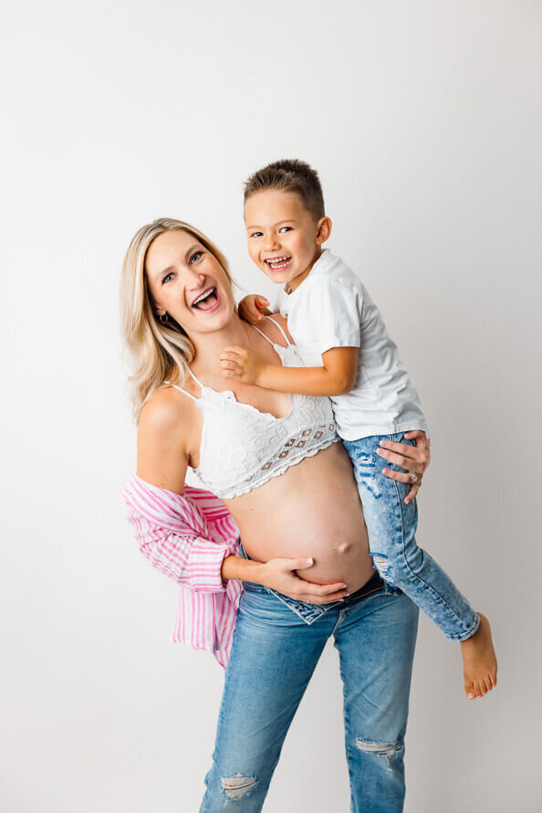 A mom and her son laugh during maternity photos in the studio.