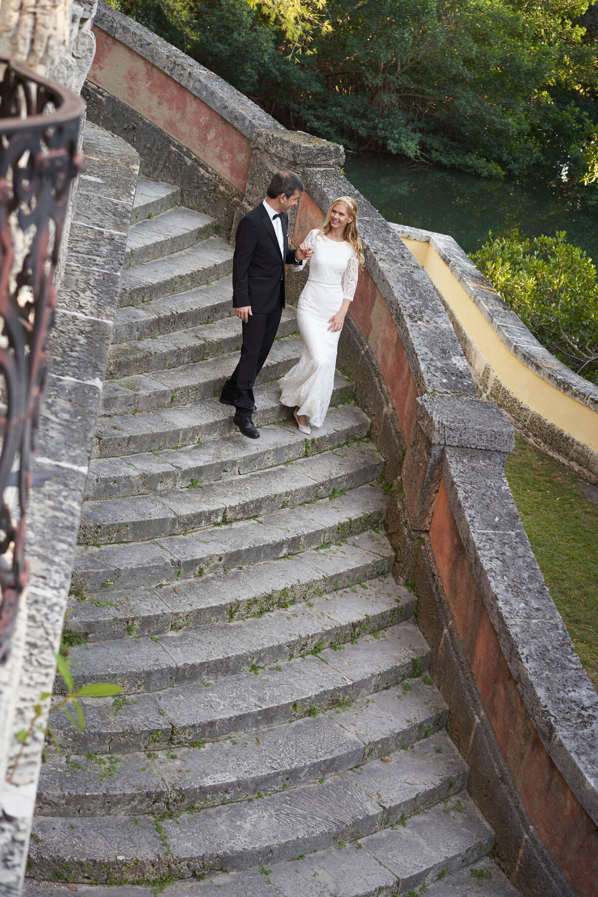 A bride and groom walk hand in hand down a stone staircase, exuding timeless elegance, captured by Rodrigo Varela Photography.