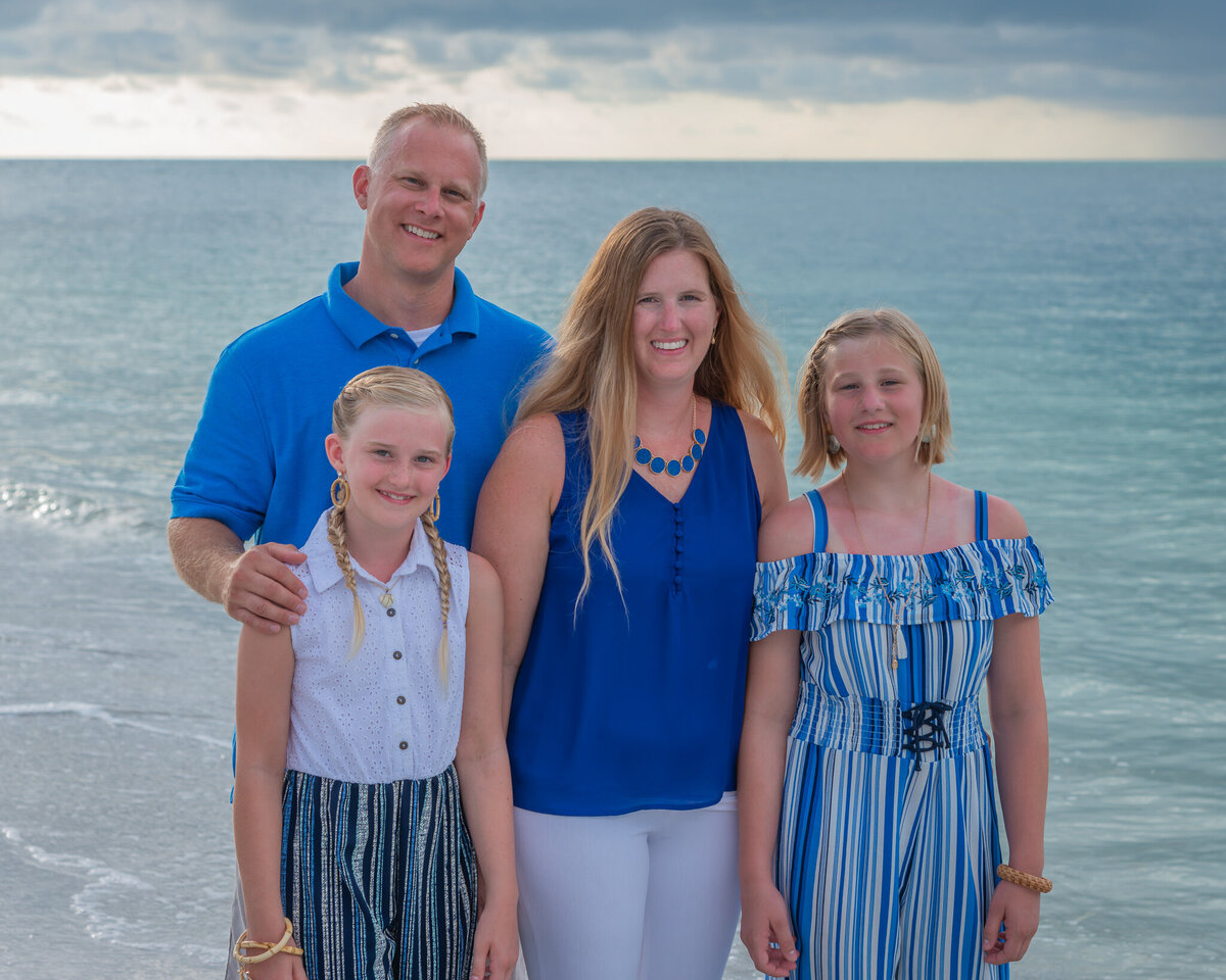 A family dressed in shades of blue pose for photos at the beach.
