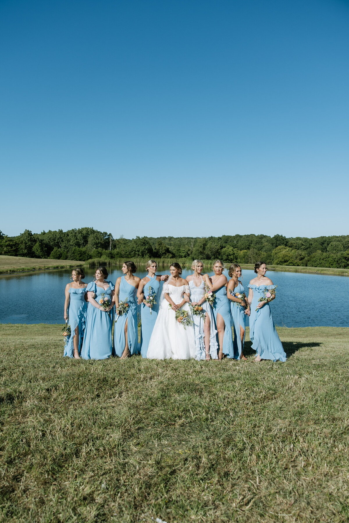 Bride and bridesmaids pose in front of outdoor water ceremony site at Willstone Acres wedding venue