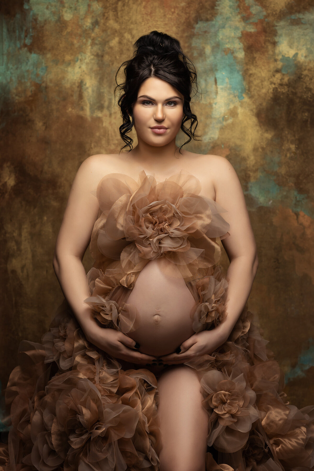 An expecting mother cradles her belly, wearing a sheer floral-adorned gown against a rich gold and teal backdrop. Captured by Dallas maternity photographer Lindsay Walden, this portrait radiates strength and beauty.