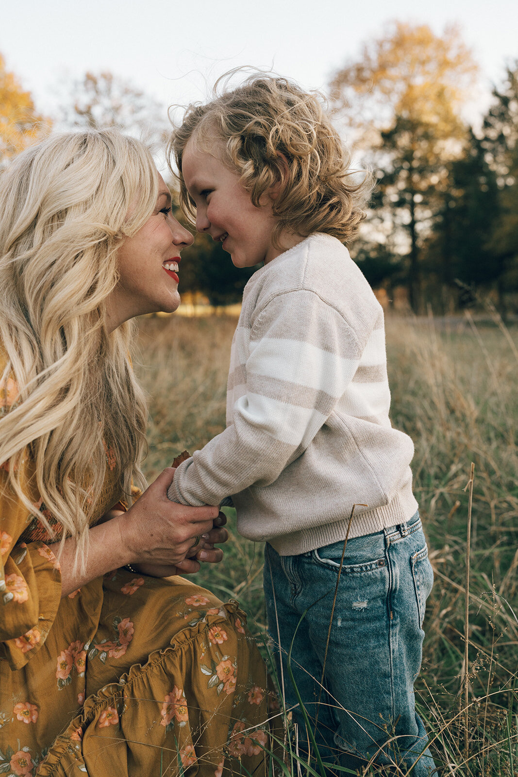 Mother kneeling down to make eye contact with her curly-haired son during an outdoor family photography session