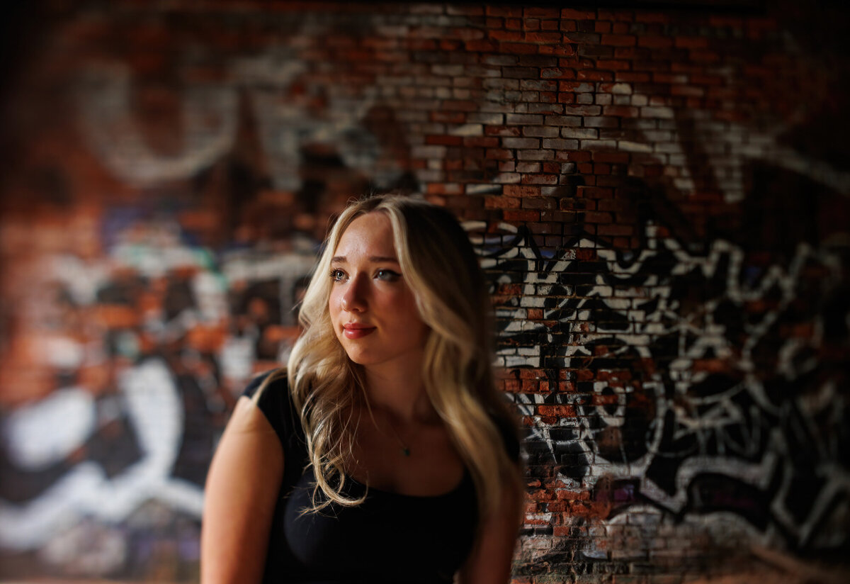 The brick wall is loaded with graffiti as Maria looks out the window.