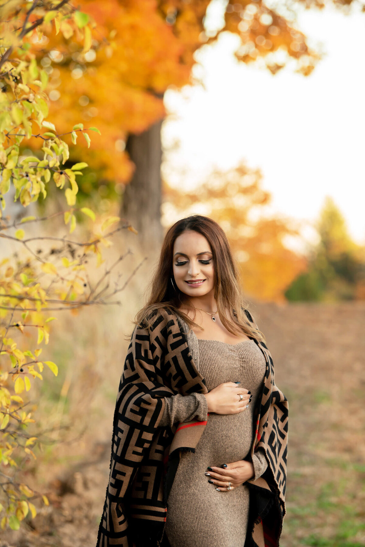 pregnant woman wearing a beige dress and shall for her outdoor fall maternity photos in Burlington, Ontario 
