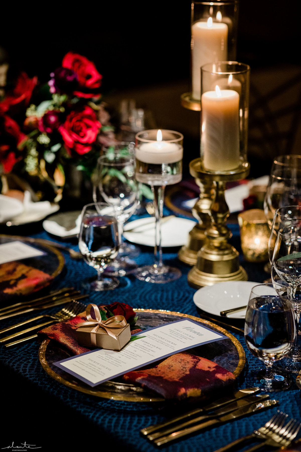 gold candle hurricanes, red flower arrangement, and place setting with red napkin at winter wedding