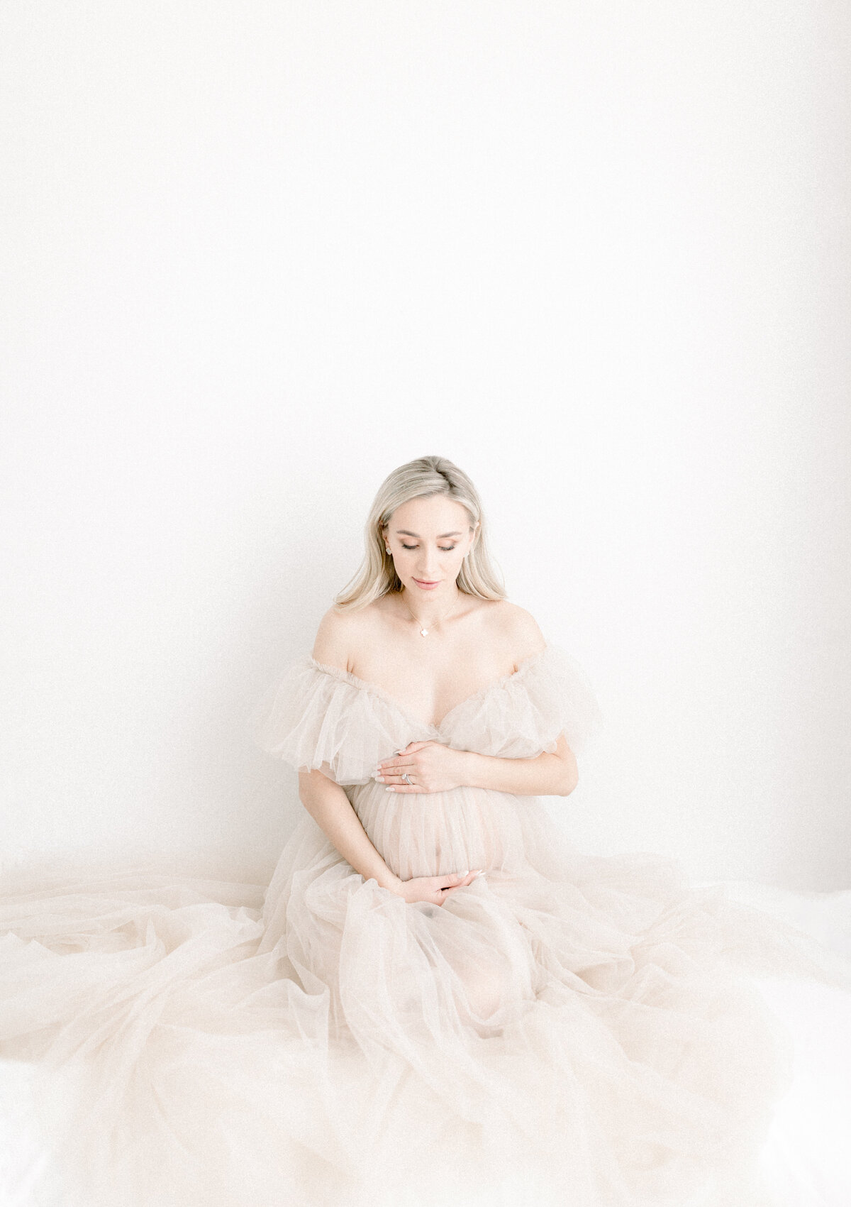 Expecting mother dressed in a beautiful tulle gown holding her belly