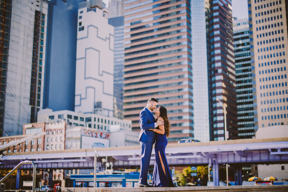A couple standing at the pier during their engagement session at the seaport district in nyc with buildings in the back