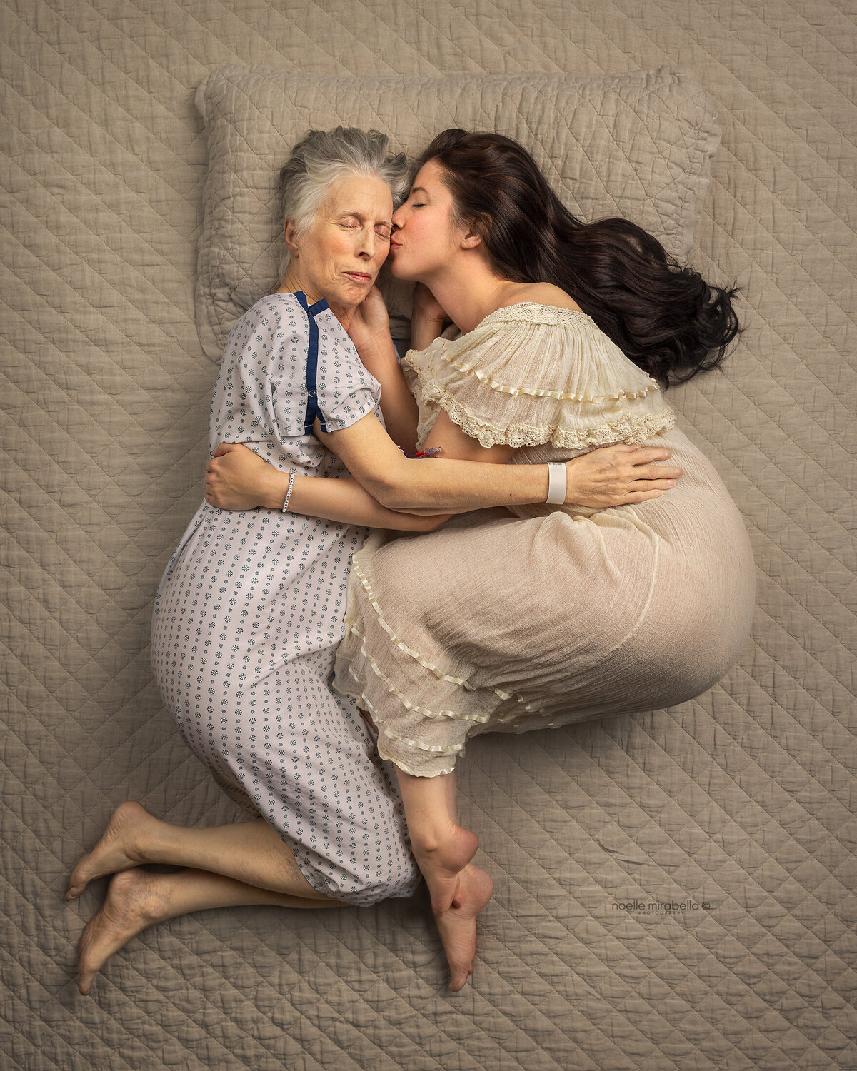 Sick elderly mother in a hospital gown, snuggling her adult daughter in bed. 