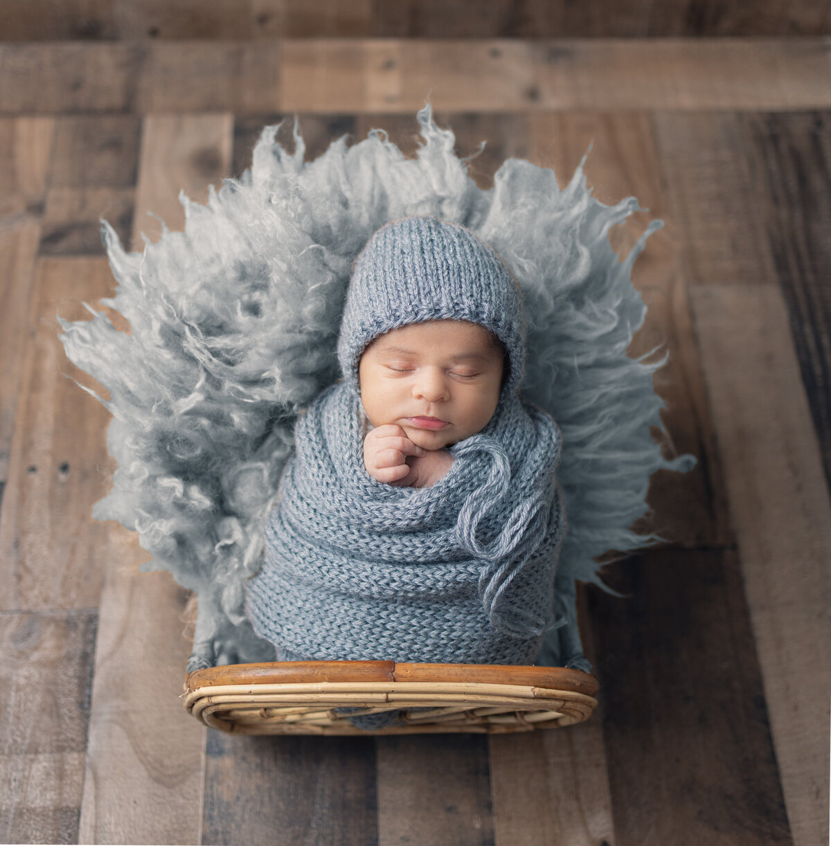 Newborn boy wrapped in gray wearing a matching bonnet laying upright in a bed supported by grey wool during a studio newborn session in Waldwick, NJ
