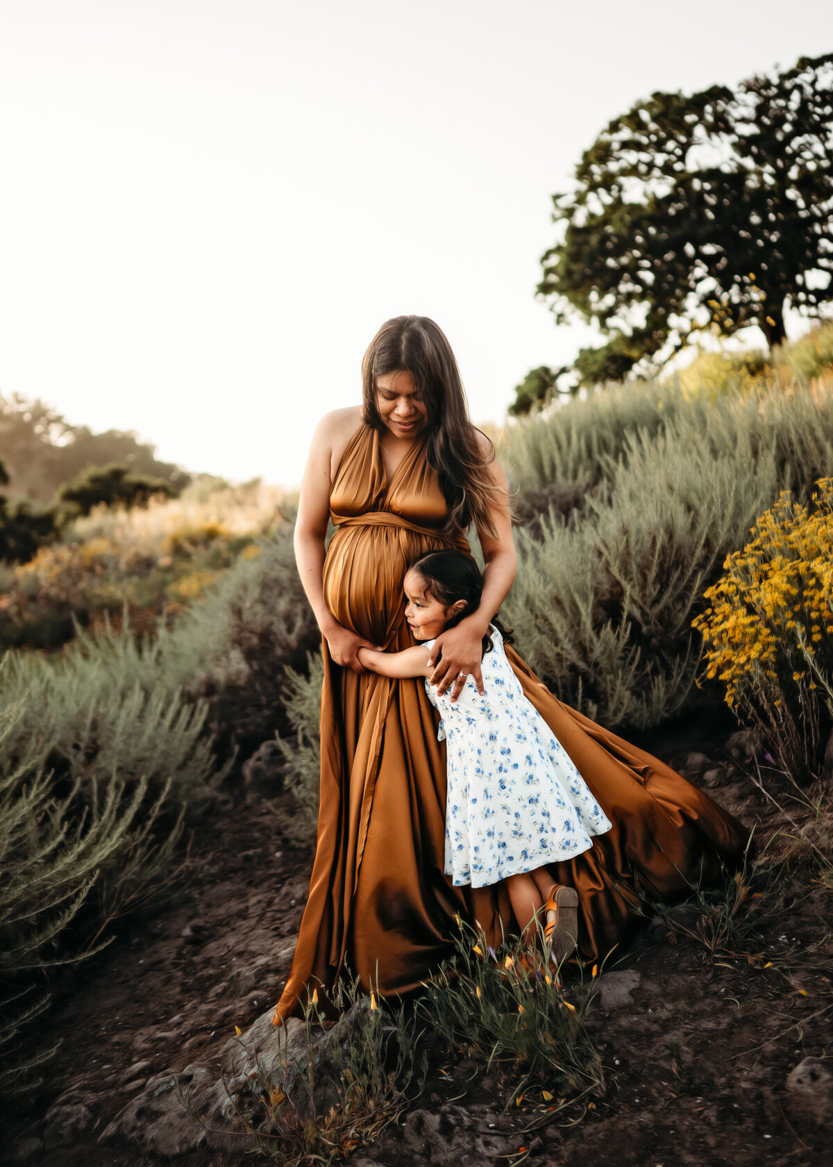 Toddler hugs pregnant mom in gold dress