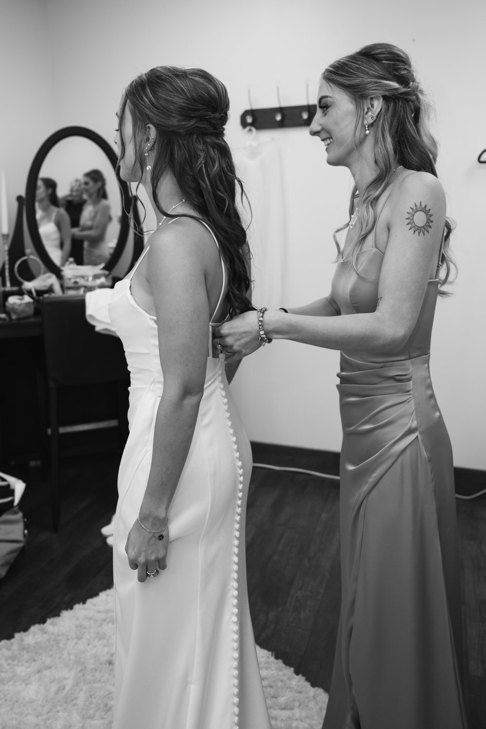 black and white image sister bridesmaid zipping up wedding dress for bride