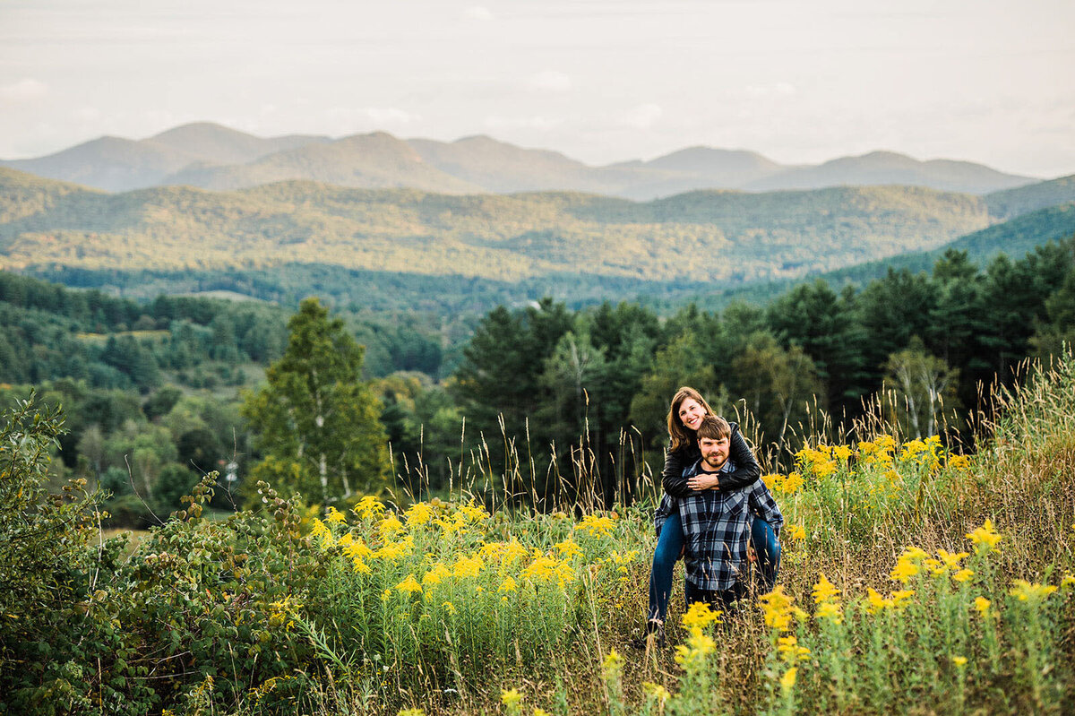 couple piggyback in field with yellow flowers at lake bomoseen lodge