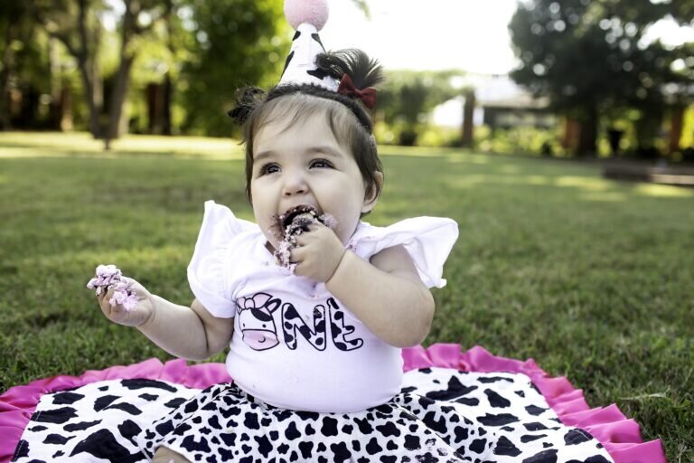 One-year-old birthday girl wearing a pink dress and playing with birthday decorations during her photoshoot