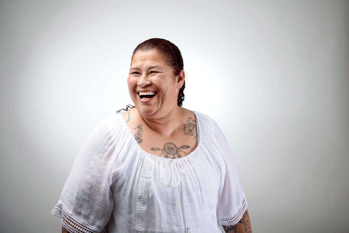 A smiling women who is homeless is photographed in studio on a white backdrop for Father Joes Villages.
