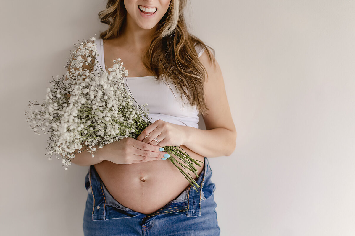 pregnant mama holding a bouquet of flowers agsint studio wall for denver maternity photos