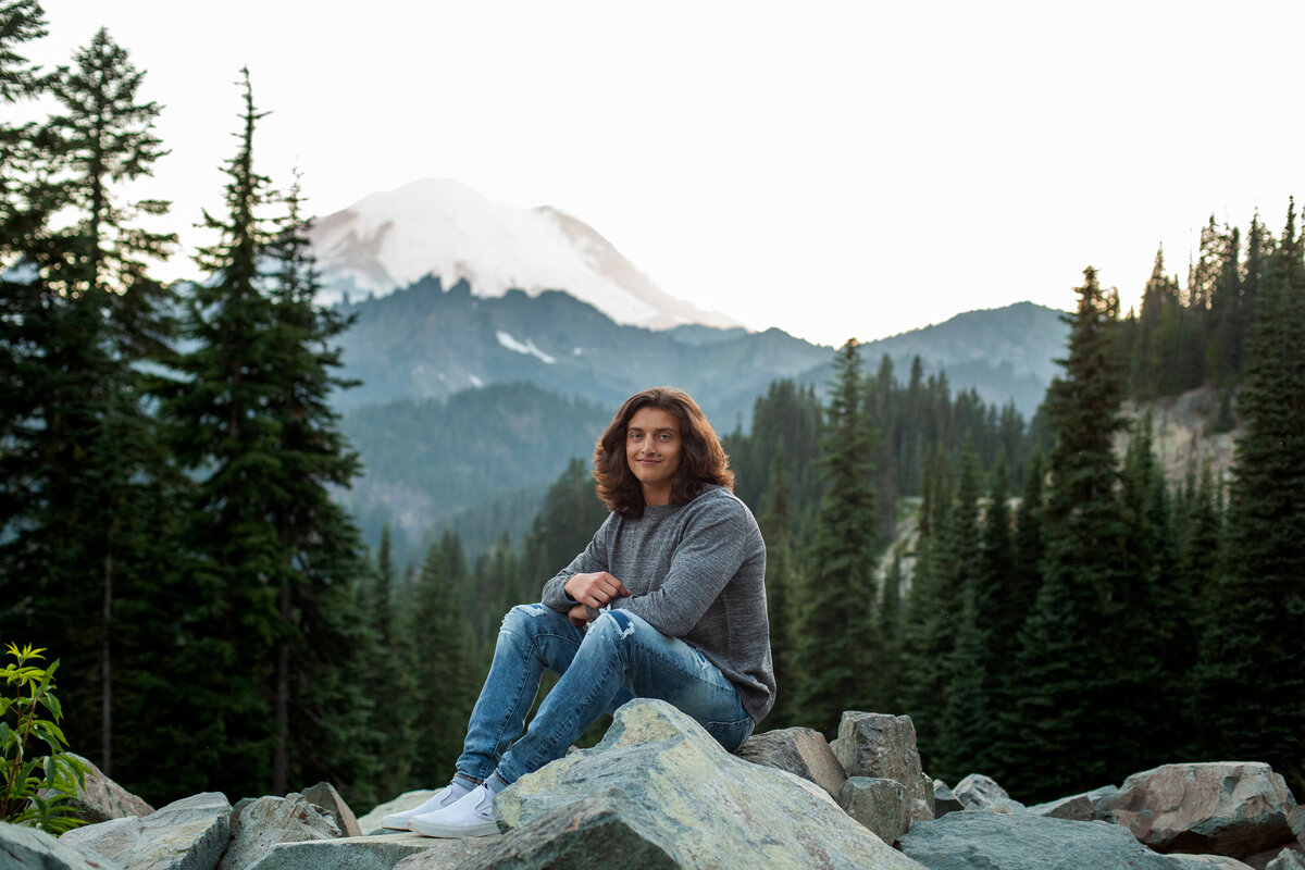 senior boy sitting on rock with mount rainier behind him at sunset