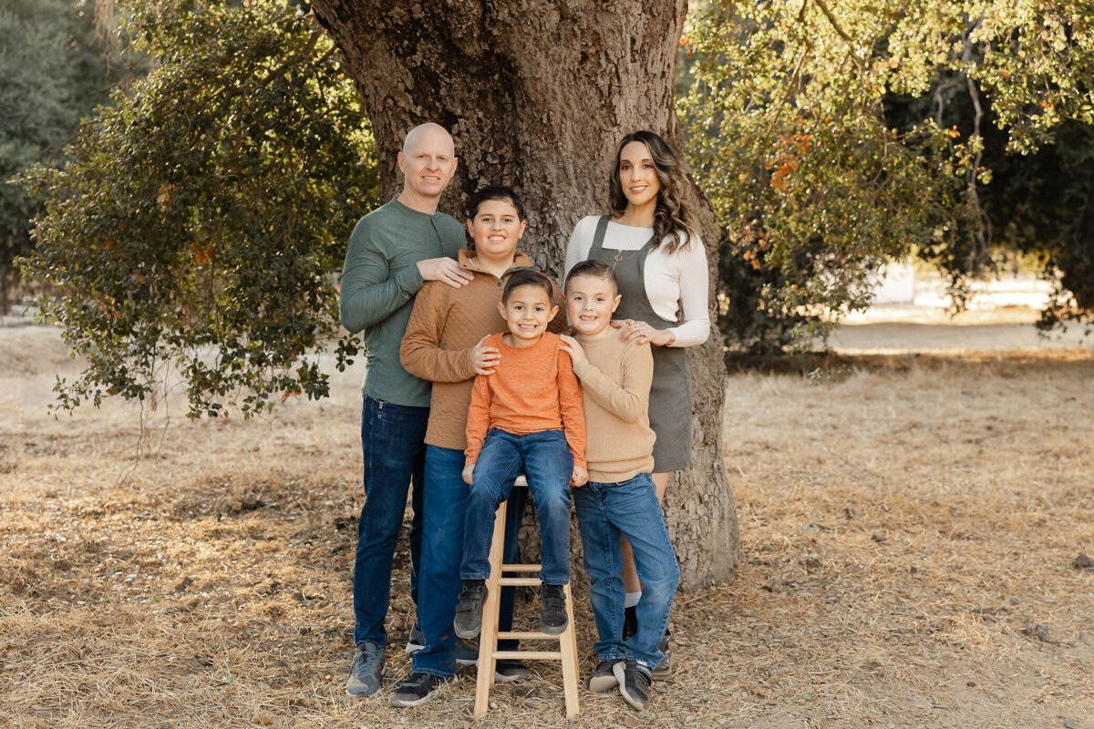 Family of five standing under a large tree in fall tones, parents with three sons. Photographed by Yucaipa family photographer Kaitlyn Dawn Photography.